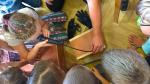 Dzieci za pomocą specjalnego sprzętu zaglądają do środka drewnianego zamkniętego pudełka