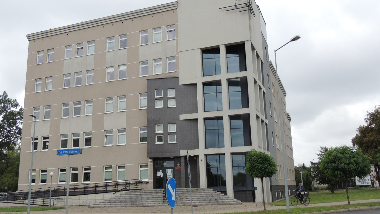 Na zdjęciu budynek w beżowo - szarej elewacji, przeszklony fragment frontu budynku