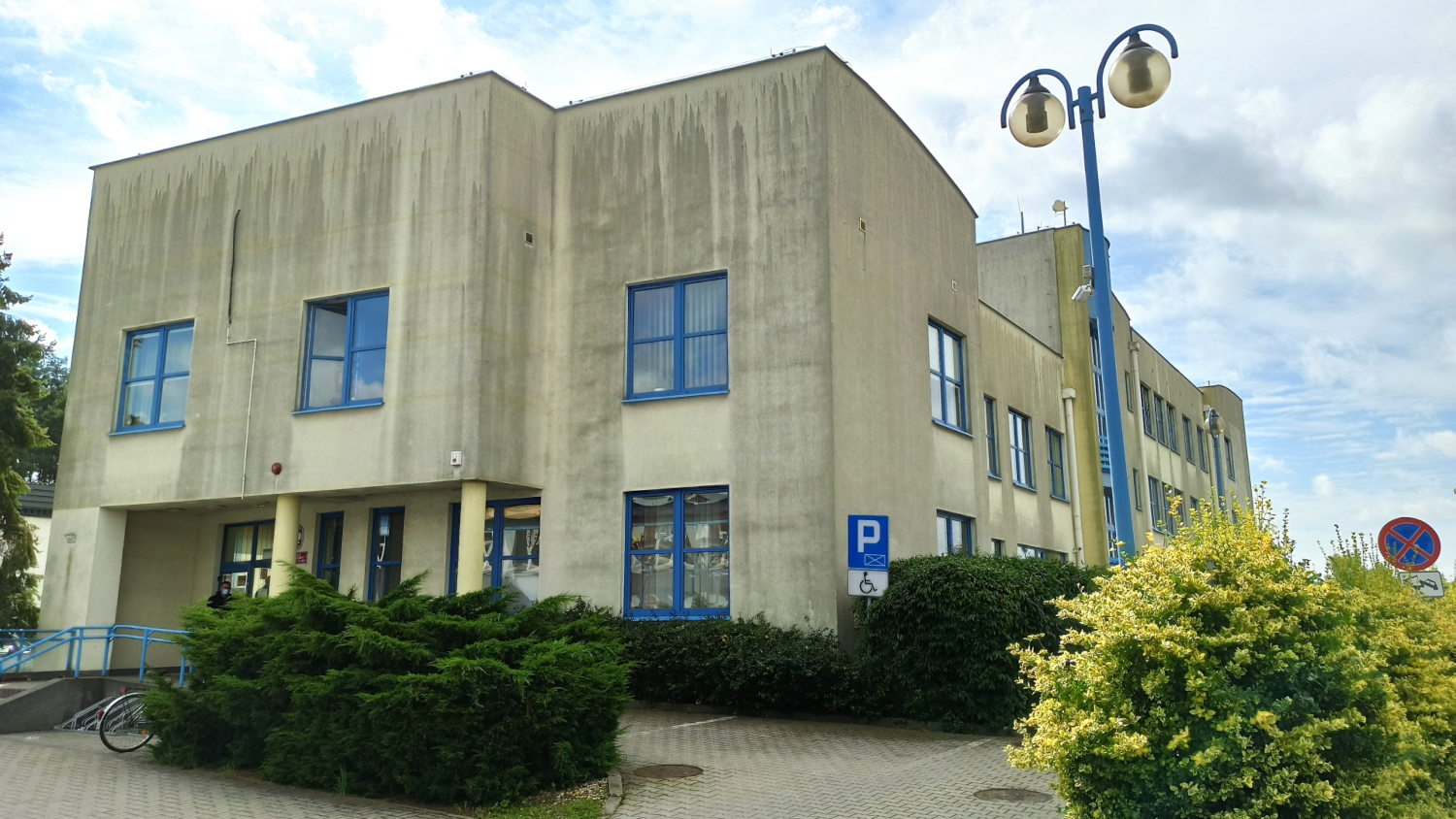 Na zdjęciu budynek w szarej elewacji, obramowania okien i drzwi w kolorze niebieskim