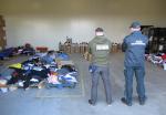 Funkcjonariusz KAS i funkcjonariusz SG stoją tyłem i patrzą na ułożone na podłodze tekstylia i obuwie