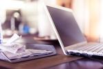 Otwarty laptop a obok kuweta z papierowymi paragonami