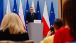 Wiceminister finansów odpowiada na pytania dziennikarzy. w tle flagi Polski oraz Unii Europejskiej 
