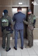 dwaj umundurowani funkcjonariusze KAS stoją z mężczyzną przed drzwiami windy w budynku prokuratury