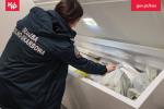 Funkcjonariuszka Służby Celno Skarbowej pokazuje ręką żywność w zamrażalce zatrzymaną na lotnisku