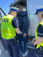 Funkcjonariusze Policji zakładają kajdanki mężczyźnie. Obok stoi bus.