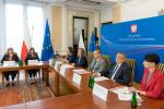 na zdjęciu stoły ustawione w kształcie litery U za stołami siedzą pracownicy Ministerstwa Finansów w tle flagi polskie i unijne 