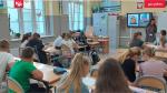 Pani prowadzi zajęcia z uczniami. młodzież coś pisze na kartkach. w tle wyświetla się prezentacja ze slajdem: dlaczego warto płacić podatki. 