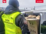 Funkcjonariusz otwiera część ładunkową busa, wewnątrz kartony z papierosami