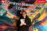 Pracownica Urzędu Skarbowego pozuje do zdjęcia na tle banneru Gminna Biblioteka Publiczna i Centrum Kultury w Dopiewie