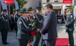 Funkcjonariusze Służby Celno-Skarbowej stoją w równym rzędzie, mężczyzna w granatowym garniturze wręcza akt mianowania w czerwonej teczce i ciemno czerwoną różę