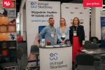 Stoisko informacyjne Krajowej Administracji Skarbowej podczas wydarzenia konferencyjnego. Za ladą oznaczoną logo e-Urzędu Skarbowego stoją trzy osoby obsługujące stoisko. W tle widoczne są roll-upy promujące e-Urząd Skarbowy oraz Krajowy System e-Faktur (KSeF), z hasłem „Wygodnie. Szybko. W każdej chwili.