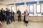 W środku sali obsługi nowego budynku ksiądz z kropidłem w ręku święci nowy obiekt, po lewej widać część gości